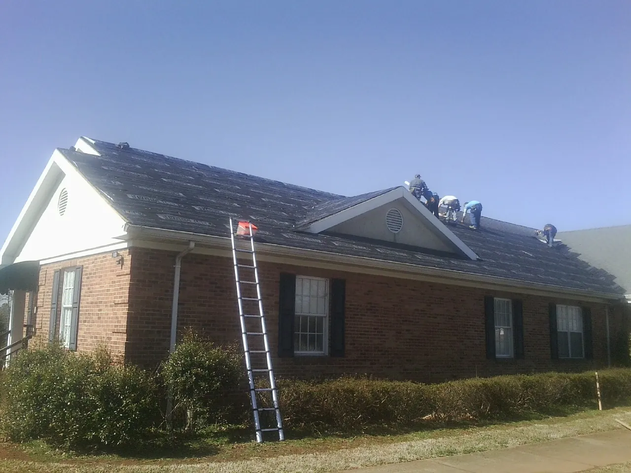 Crew tearing shingles off a brick ranch roof with a ladder set — Metal Roof Repair work by our crew in Roaring Gap