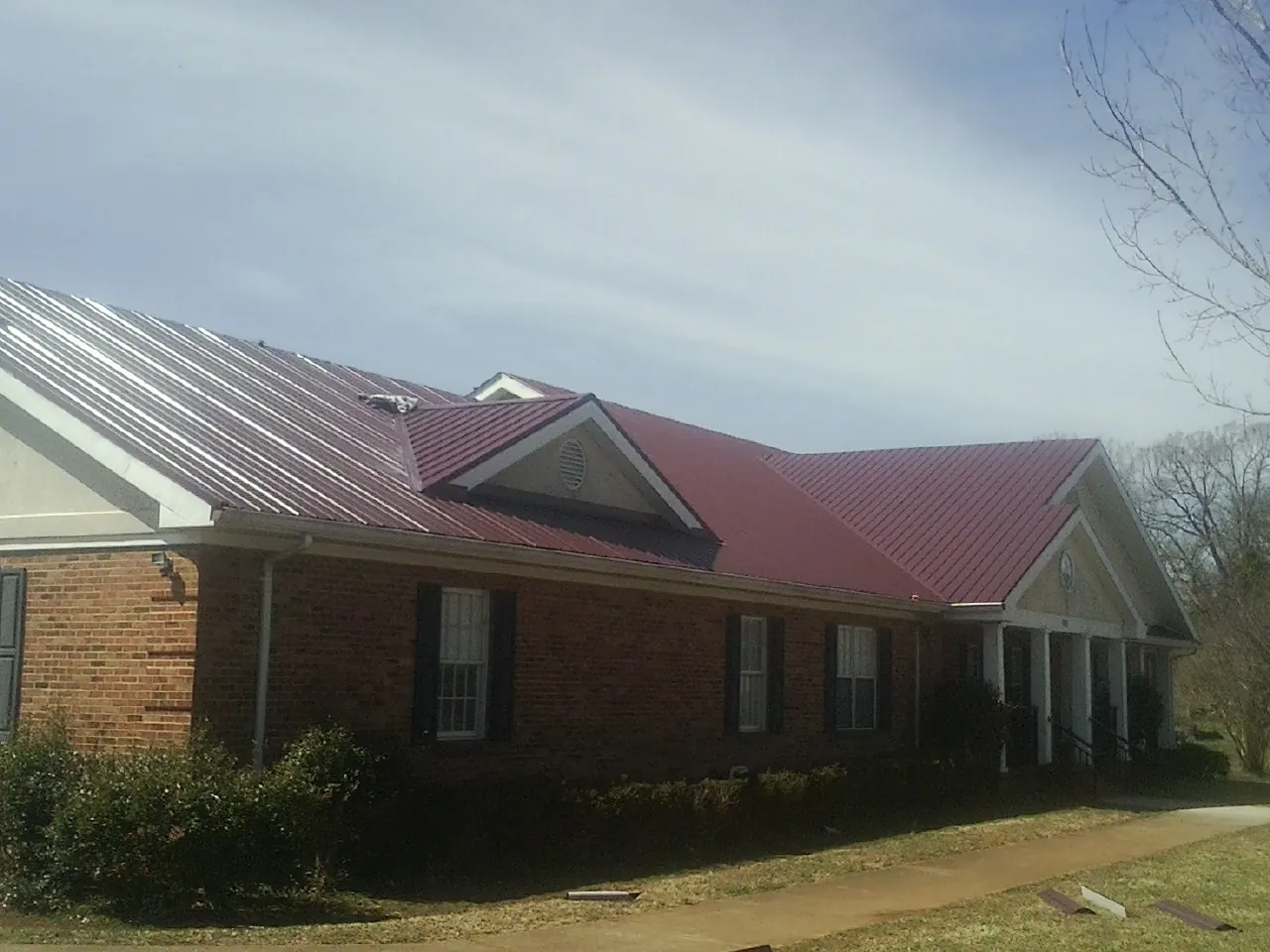 Red metal roof with gabled entries on a long brick building, from a Hail Damage Roof Repair job in Roaring Gap