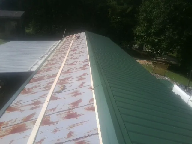 Old rusted panels beside newly installed green metal roofing — Wind Damage Roof Repair by Roofing Brothers in Roaring Gap