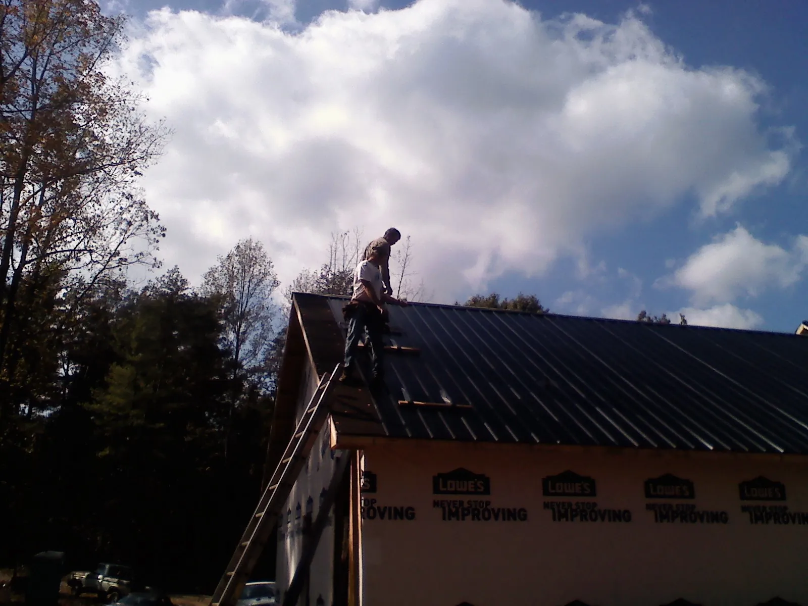 Roofer fastening dark metal panels high against a cloudy sky, from a Roof Inspection job in Roaring Gap