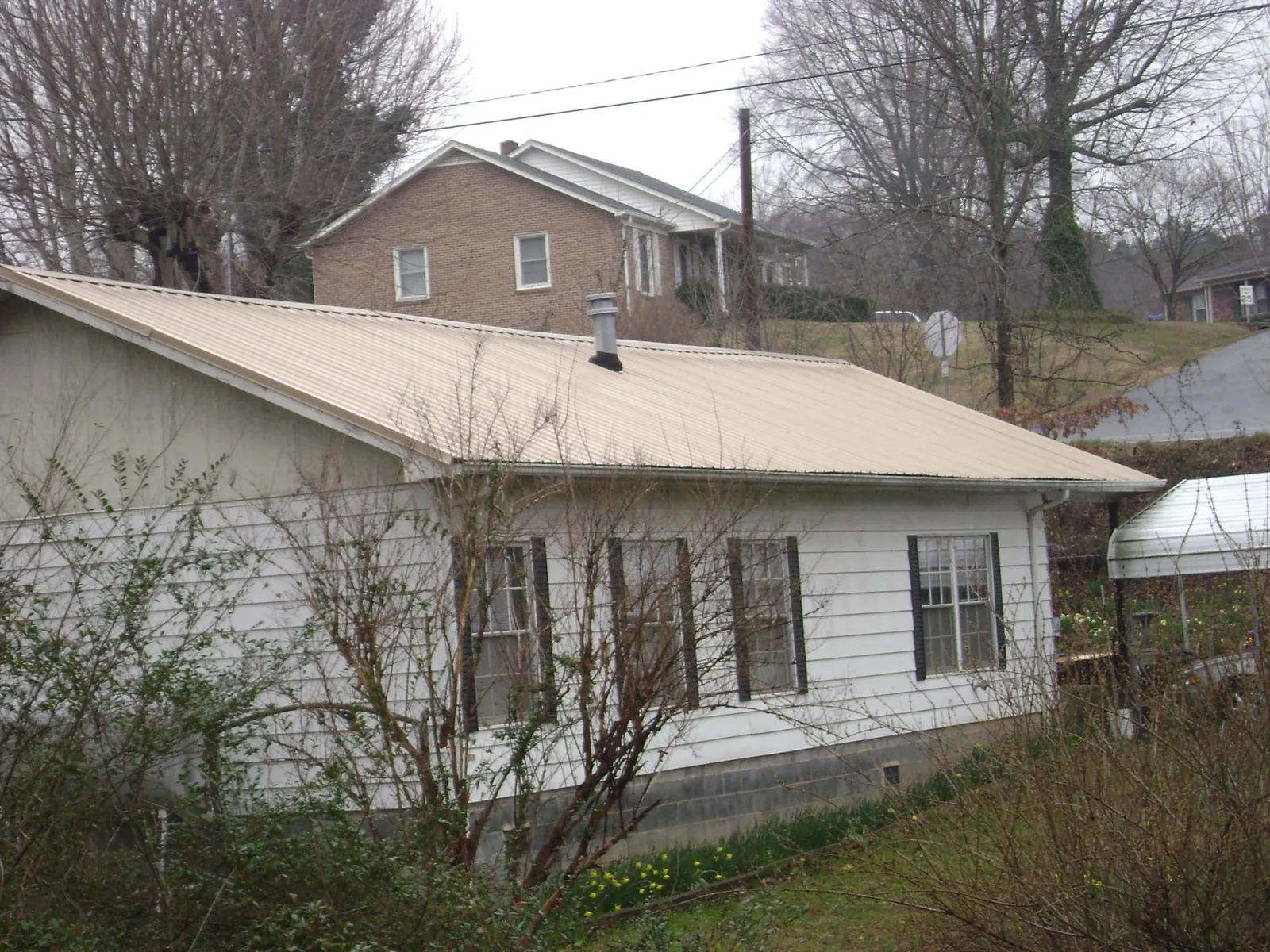 Tan metal roof on a white sided house set into a hillside — Commercial Roofing by Roofing Brothers in Roaring Gap